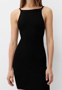 Black ribbed dress with thin spaghetti straps and a fitted silhouette. Features a straight neckline and a mid-thigh length. Smooth texture.