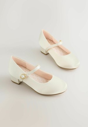 Pantofi Mary Jane din piele ecologică albă, cu vârf rotund, toc mic și o curea decorativă cu accent de nasture auriu.