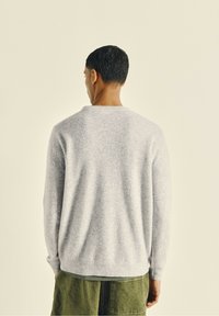 Un pull en laine grise avec une texture douce, un col rond et des manches longues, associé à un pantalon en velours côtelé olive, vu de dos.