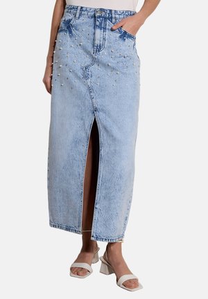 Falda de mezclilla azul claro con abertura frontal y pequeñas decoraciones de perlas, combinada con sandalias blancas de tacón.