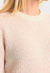 Ljust rosa tröja med ribbad halsringning och en strukturerad mönster av små prickar. Mjuk, stickad tyg med en subtil glans.