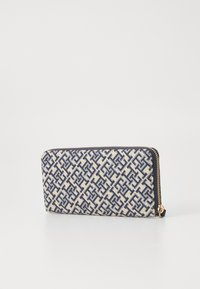 Canvas zip wallet with a geometric blue and cream pattern, featuring a gold zipper and black leather accents. Sturdy and compact design.