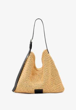 Natural woven straw tote bag with a textured surface, large open top, curved shape, and a dark leather strap. Features a black accent at the base.