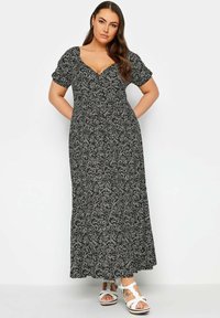 Abito lungo in tessuto nero con motivo floreale bianco, caratterizzato da scollo a V, maniche corte a sbuffo e una silhouette fluida. Abbinato a sandali bianchi.