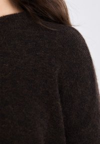 Brown knitted sweater with a textured surface, featuring a crew neckline and short sleeves. The fabric appears soft and warm.