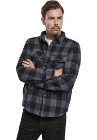 Camisa de franela a cuadros en negro y gris, con dos bolsillos en el pecho, cierre de botones y cuello. La tela parece suave y texturizada.