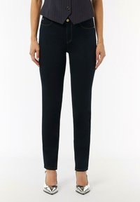 Schmal geschnittene dunkelblaue Jeans mit kontrastierenden gelben Nähten, fünf Taschen und einem klassischen Knopfverschluss. Glatte Denim-Textur.