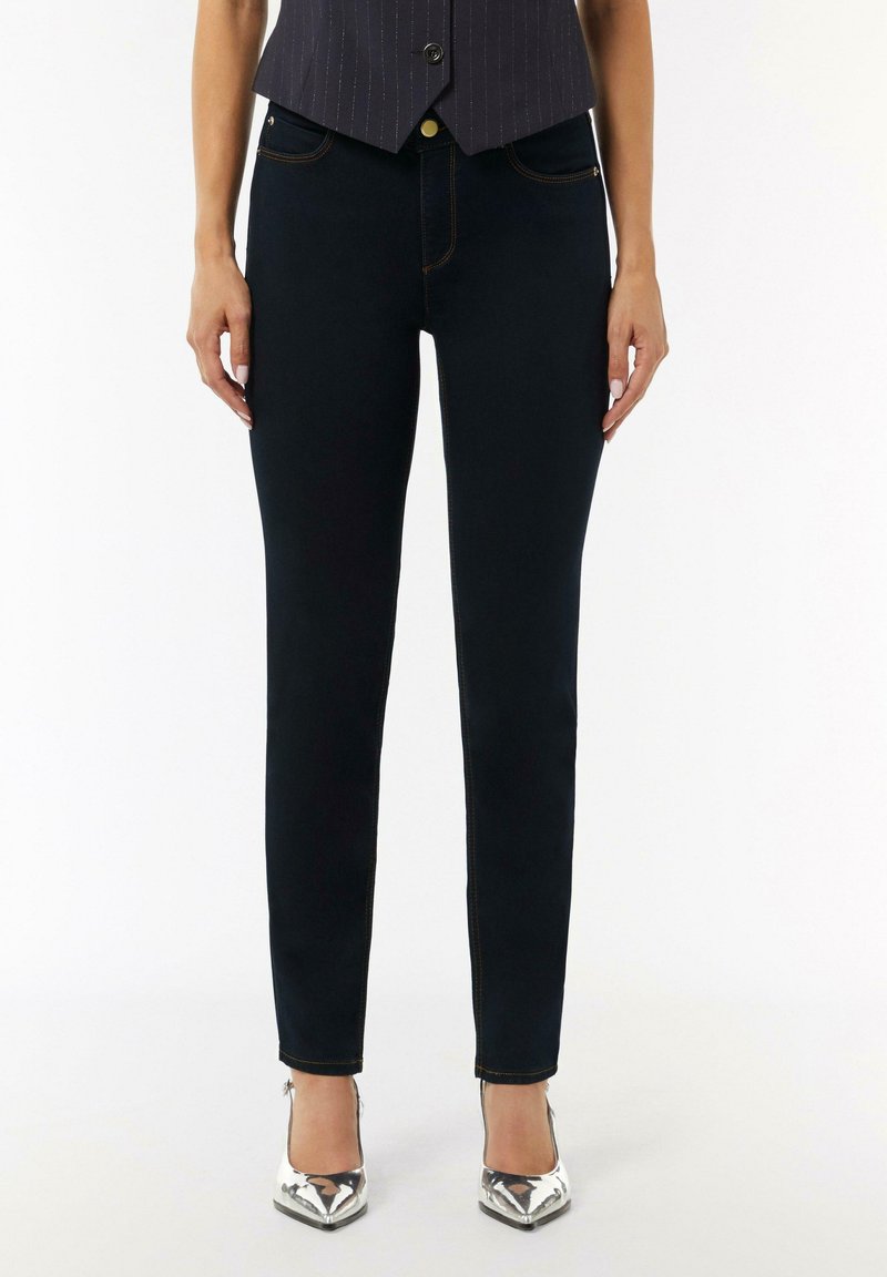 Schmal geschnittene dunkelblaue Jeans mit kontrastierenden gelben Nähten, fünf Taschen und einem klassischen Knopfverschluss. Glatte Denim-Textur.