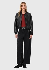 Chaqueta bomber de cuero negro con puños acanalados, usada sobre una camisa roja. Combinada con vaqueros negros de talle alto y botines negros.