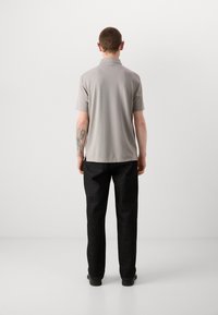 Lys grå polo skjorte med korte ermer og rett hem, kombinert med mørke denimbukser. Enkelt design, glatt tekstur, ingen synlige mønstre.