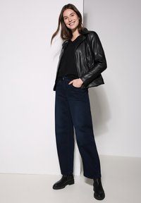 Veste en cuir noire, haut noir, jeans en denim bleu foncé avec jambes larges, et bottines noires. Texture lisse avec peu de matériel et des lignes de design épurées.