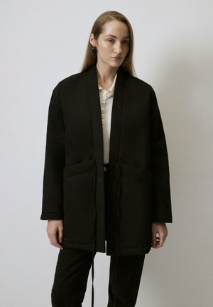 Crni kimono-stil jakna s teksturiranim završetkom, s vezivanjem na mašnu, dva prednja džepa i širokim rukavima. Nosio se preko svijetle bluze.