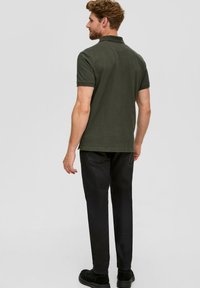Polo shirt vert foncé à manches courtes, avec un tissu légèrement texturé et des aérations sur les côtés, associé à un pantalon slim noir et des chaussures noires.