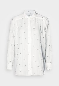 Chemise blanche à manches longues avec des rayures verticales et de petites broderies florales. Elle possède un col boutonné et une coupe standard. Tissu doux au toucher.