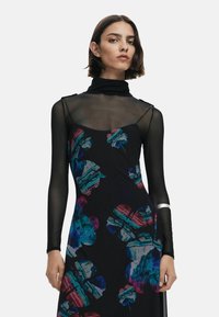 Abito nero a fiori con maniche lunghe trasparenti; presenta motivi floreali colorati in blu e rosa; colletto alto, tessuto morbido, design aderente.
