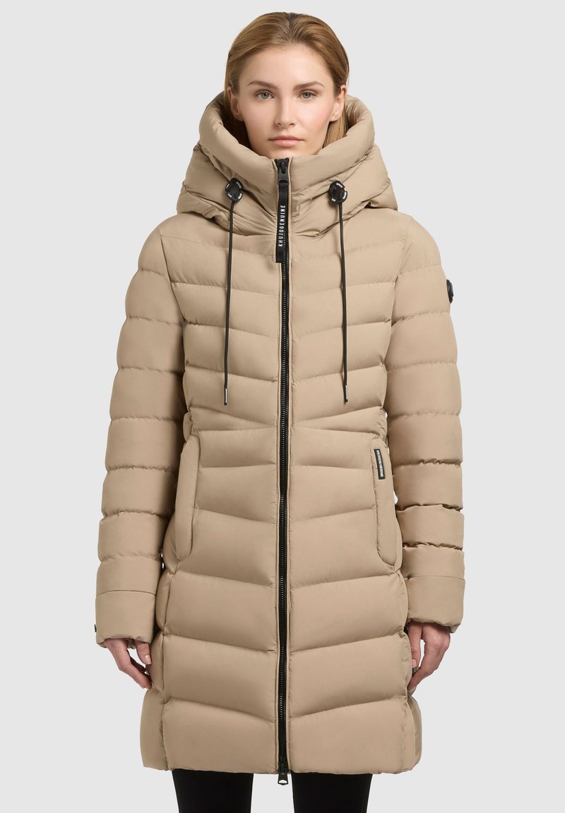 Beige pufferjas met een hoge kraag, ritssluiting en trekkoorden. Beschikt over een gestikt ontwerp en zijzakken. Glad textiel.
