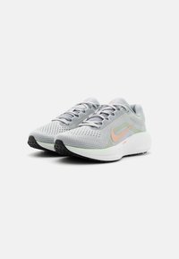Baskets de course Nike gris clair avec un swoosh pêche, tige en mesh, semelles épaisses blanches et semelles extérieures noires, présentées côte à côte sur un fond blanc.