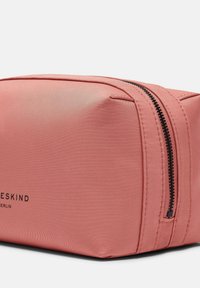 Rosa kosmetiktasche aus Stoff mit rechteckiger Form, ausgestattet mit einem schwarzen Reißverschluss und einem bedruckten Logo auf der Seite. Glatte Textur, minimalistisches Design.