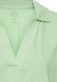 Mintgroene organische katoenen poloshirt met een V-halsontwerp en ribbelkraag. Toont een zachte, gladde textuur met subtiele stofvariaties.