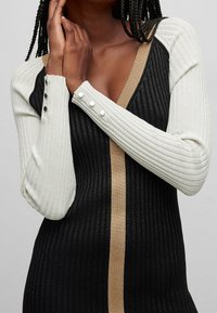 Robe en maille côtelée avec manches longues en noir et blanc, avec un accent doré au centre et des boutons décoratifs sur les manches.