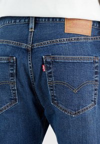 Donkerblauwe denim jeans met een hoge taille, voorzien van twee achterzakken, contrasterende stiksels en een leren logopatch op de tailleband.