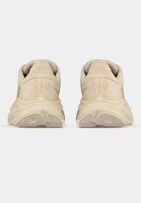 Béžové sportovní boty s texturovaným síťovaným svrškem, polstrovanou podešví a minimálním zdobením. Mají silnou podrážku a nenápadné logo.