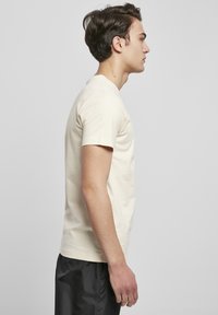 Roomkleurige katoenen t-shirt met korte mouwen en een ronde hals, zijwaarts getoond. De stof lijkt glad en zacht.