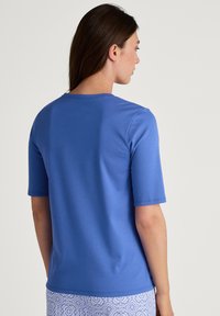 Blauwe t-shirt met korte mouwen, ronde hals, zachte stof, gladde textuur. Van de achterkant gezien, gedragen met een patroonachtige onderkant.