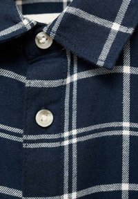 Camicia a scacchi blu navy con colletto button-down, motivo a quadri bianchi e un bottone di plastica trasparente al colletto. Tessuto morbido.