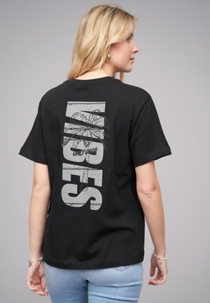 T-shirt en coton noir avec un grand graphisme blanc de palmiers et le texte "ONLY GOOD" en vertical au dos. Coupe classique.
