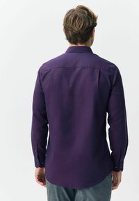 Koszula z długim rękawem w głębokim fioletowym kolorze o gładkiej fakturze, z zapięciami na guziki przy mankietach oraz prostym dołem, z klasycznym kołnierzykiem i yoke z tyłu.
