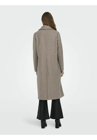 Manteau long en mélange de laine gris clair, texturé, avec un col cranté et une coupe droite, vu de dos, associé à un pantalon noir évasé.