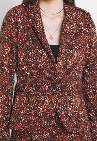 Leopardmönstrad blazer i röd, svart och krämfärgad; har en enknappsstängning och en strukturerad passform med två framfickor.