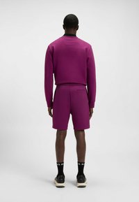 Purple sweatshirt with black collar, paired with matching shorts. Notable features include smooth texture and a rear pocket detail.