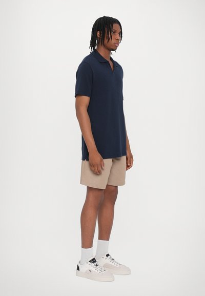 Polo de marina de manga corta, combinado con pantalones cortos beiges. Los accesorios incluyen zapatillas blancas y calcetines. Diseño sencillo, sin patrones visibles.