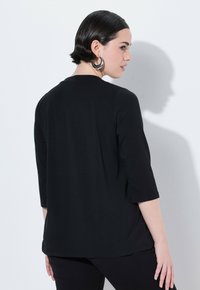 Černý přiléhavý top s třičtvrtinovými rukávy a kulatým výstřihem, vyrobený z hladké látky. Zobrazený zezadu, s minimálními detaily.