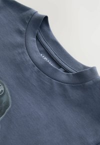 T-shirt in cotone blu navy con scollo rotondo, texture liscia e logo circolare sul lato sinistro anteriore. Design semplice senza motivi.