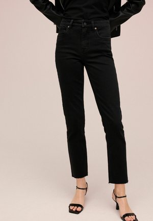 Zwarte high-waisted jeans met een rechte snit, voorzien van een ruwe zoom en subtiele stikseldetails, gecombineerd met zwarte bandjeshakken.