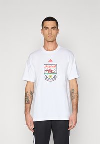 Wit katoenen T-shirt met korte mouwen en een kleurrijk Arsenal-logo gedrukt op de voorkant. Geaccentueerd met een Adidas-logo boven het ontwerp.