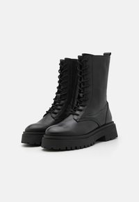 Černé kožené kotníkové boty s kulatou špičkou, předním šněrováním a robustní, texturovanou gumovou podrážkou. Na zadní straně je poutko.