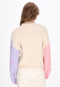 Maglione a righe beige chiaro con maniche oversize nei colori pastello lavanda e rosa, con accenti floreali ricamati sulle maniche.