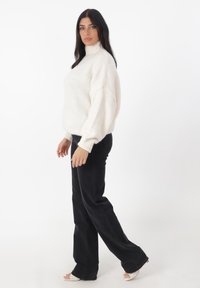 Witte gebreide coltrui met een ontspannen pasvorm, gecombineerd met zwarte flared jeans. De trui heeft geribde manchetten en een gestructureerde afwerking.