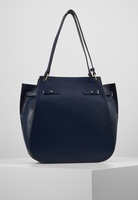 Tummansininen nahkainen kassilaukku, jossa on teksturoitu pinta, varustettu kahdella yläkahvalla, kultaisilla metalliosilla ja tilavalla avoimella muotoilulla.