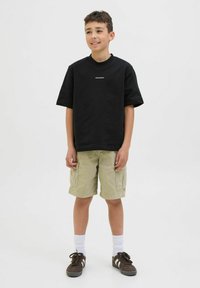 Maglietta nera a maniche corte con testo bianco, abbinata a pantaloni cargo beige. Sneakers marroni e calzini bianchi completano l'outfit. Sfondo neutro.