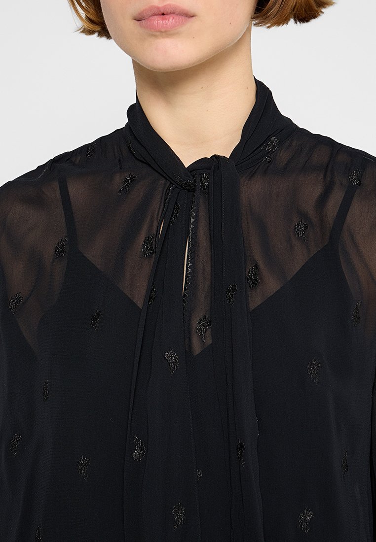 Schwarze transparente Bluse mit bestickten floralen Mustern, einem Bindeband am Ausschnitt und einem leichten, strukturierten Stoff.