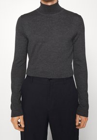 Pull à col roulé gris en tissu côtelé doux, avec des manches longues et une coupe ajustée, associé à un pantalon foncé.