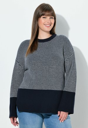 Mörkblå och vit randig stickad tröja med ribbad fåll och mudd, som har en lös passform och båtringning. Kombinerad med ljusblå jeans.