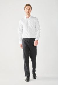 Camicia bianca a maniche lunghe con bottoni, pantaloni eleganti neri e scarpe nere. Tessuto morbido, vestibilità su misura e design semplice senza motivo.