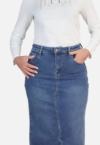 Falda de denim con cintura alta, costura frontal y dos bolsillos laterales. Color azul oscuro, tela de peso medio y textura suave.