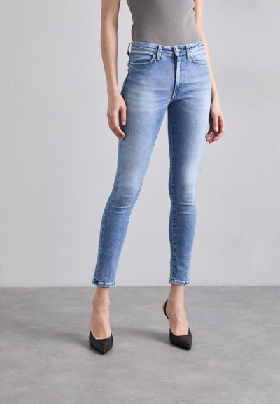 Skinny jeans in lichtblauwe denim met een vervaagde was, met een middelhoge tailleband en een versleten zoom, gecombineerd met zwarte puntige hakken.